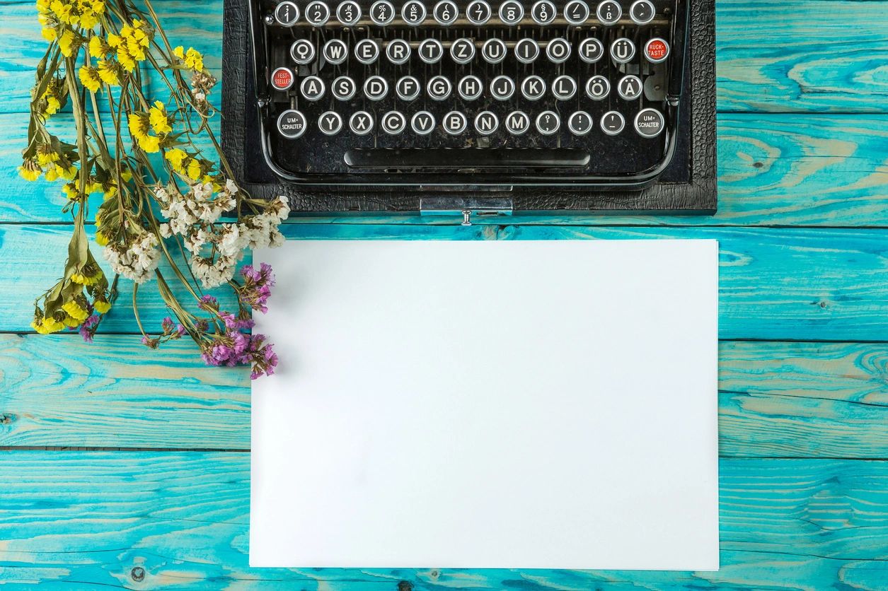 Vintage typewriter with dried flowers on turquoise surface